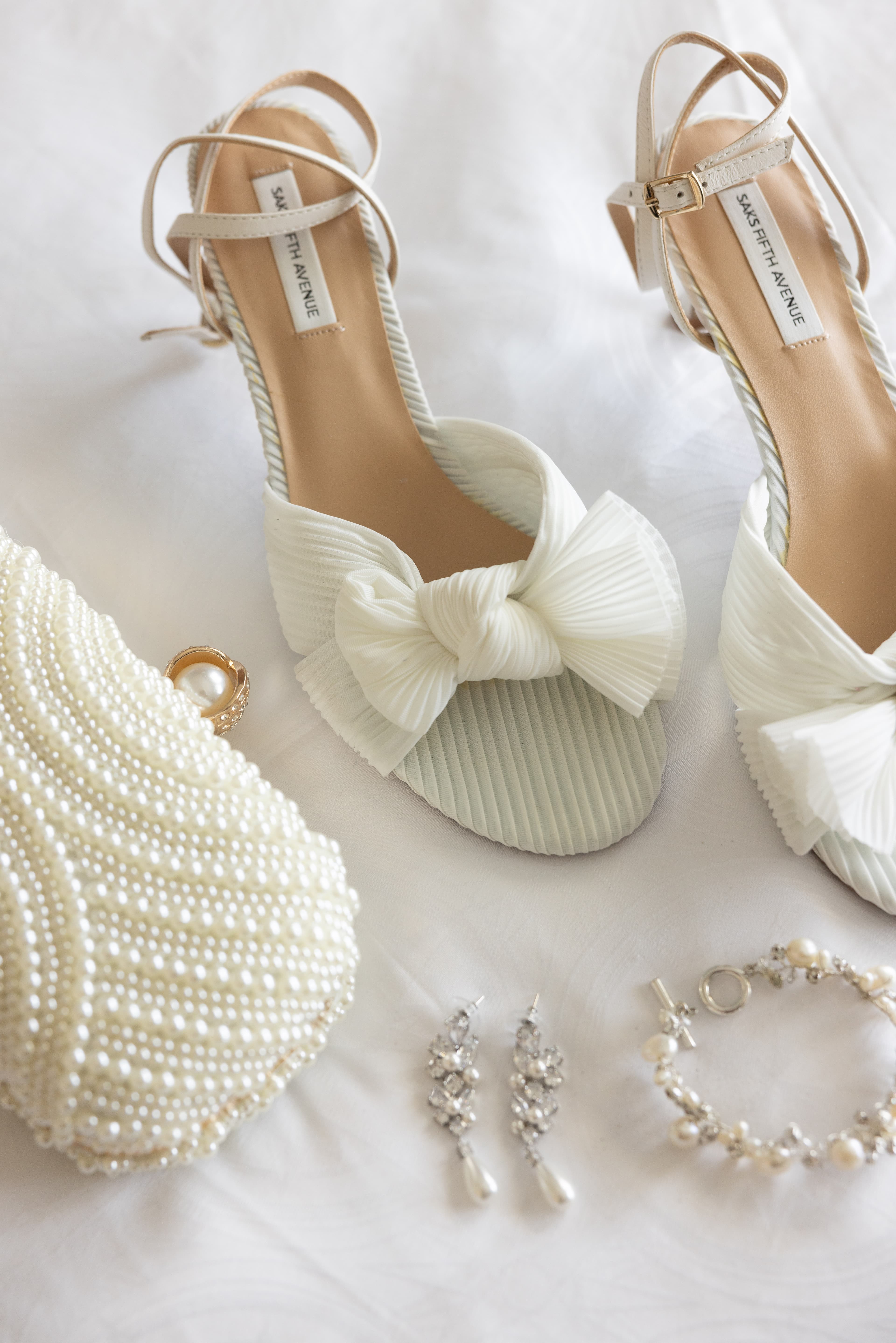 Bridal details flat lay — pearl clutch, crystal drop earrings and ivory bow heels laid out before the ceremony
