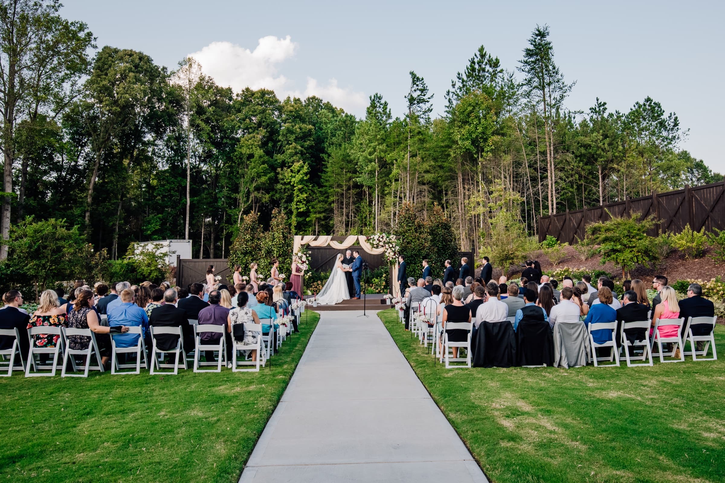 Lawn ceremony with a draped arbour and white folding chairs against the treeline — Sweet Magnolia Estate