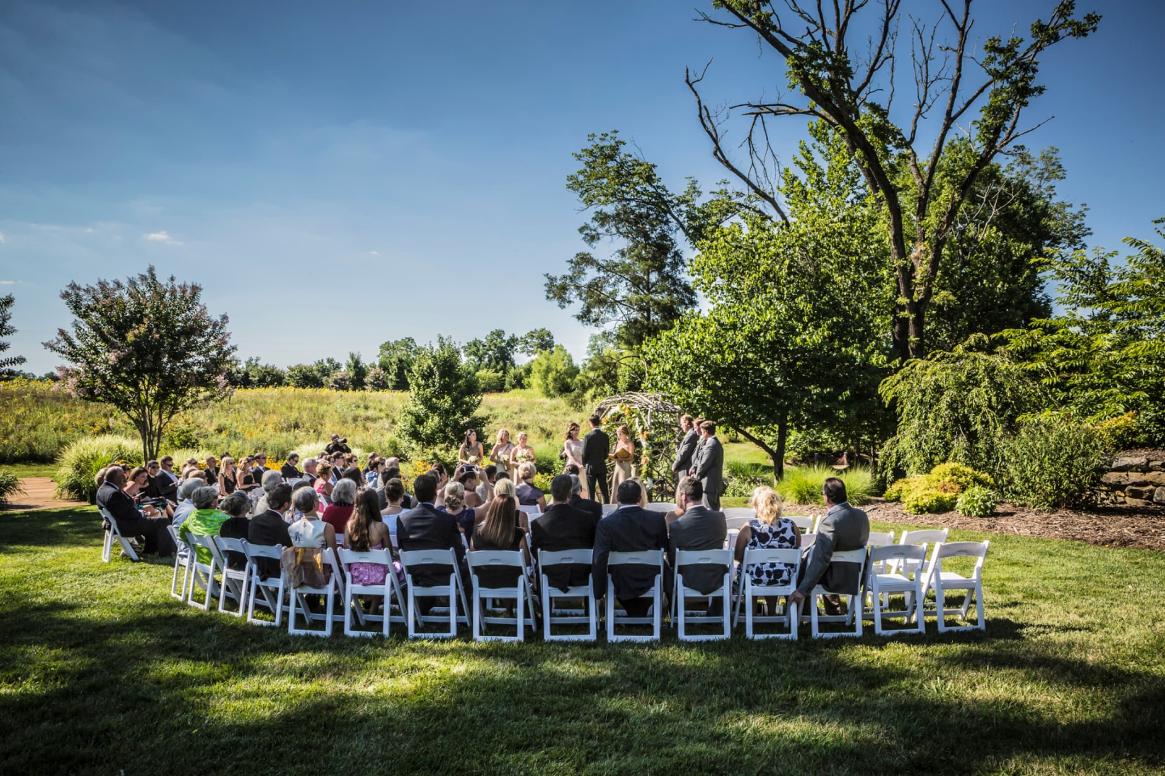 Meadow ceremony with white folding chairs and a woven arbour — The Arbors wedding venue, Cleveland, North Carolina