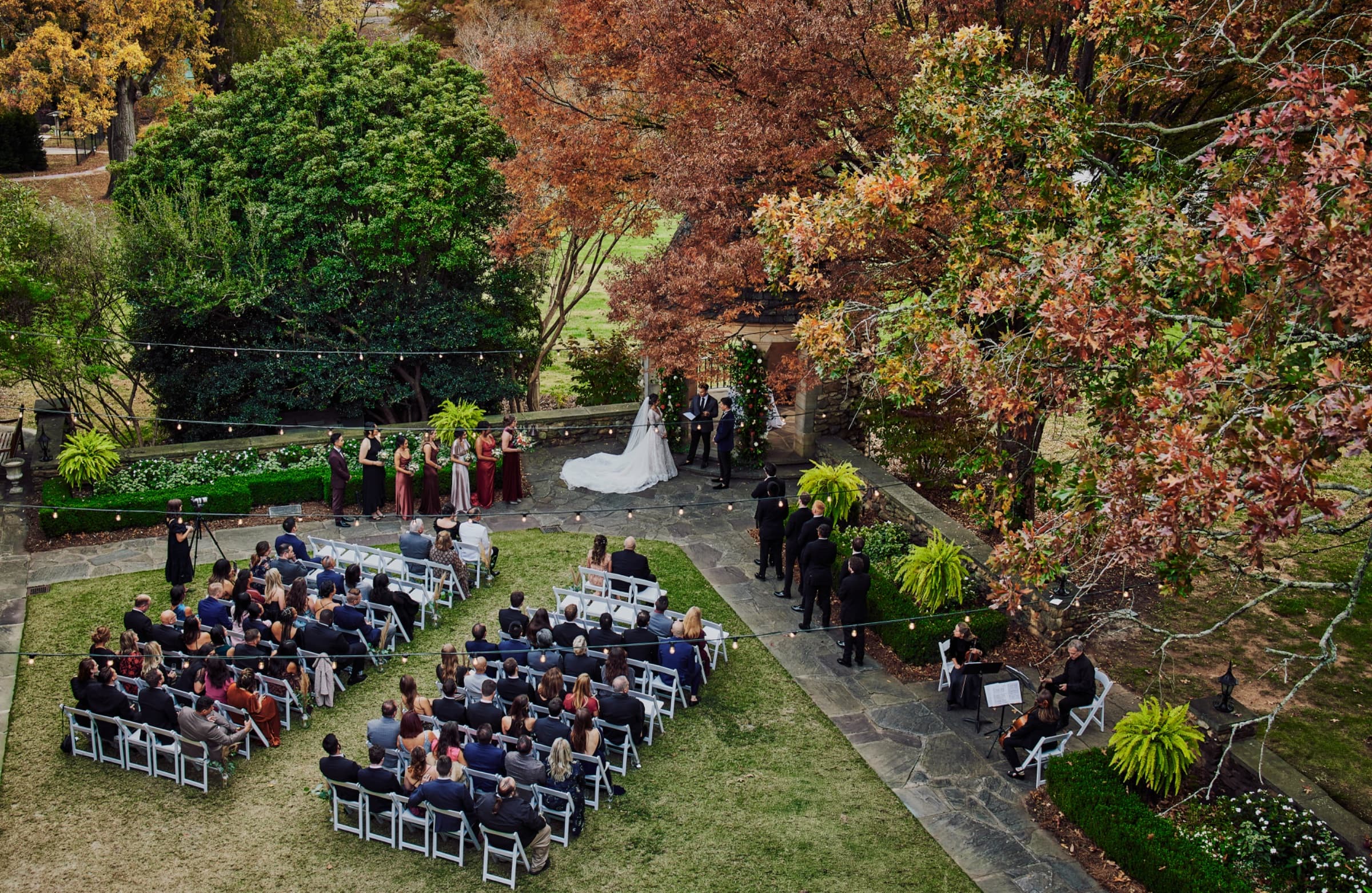 Garden ceremony under string lights ringed by autumn foliage — The Graylyn Estate