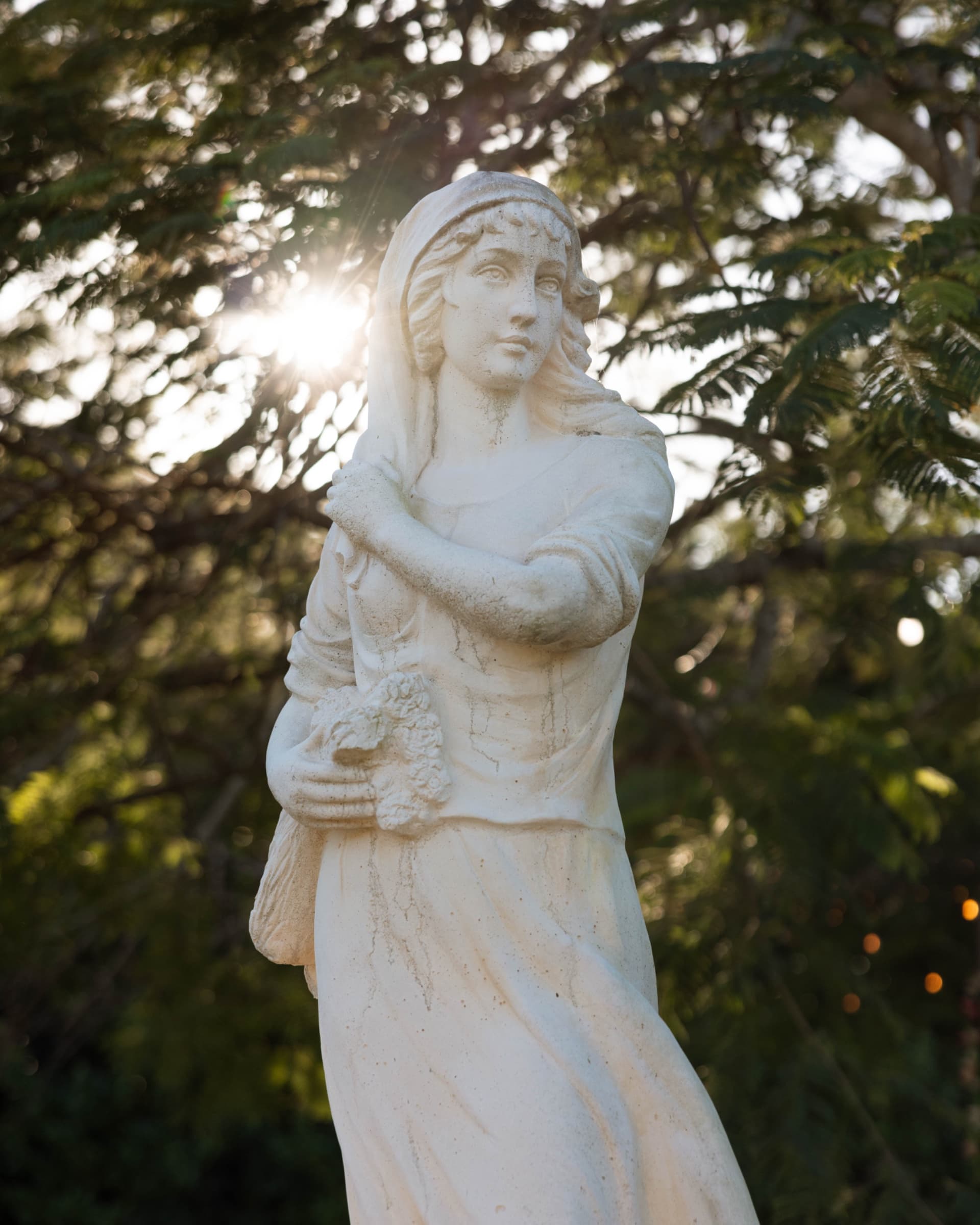 Garden statue backlit at golden hour with sun flare through the canopy — Villa Toscana Miami